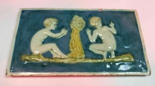 A Della Robbia rectangular tile depicting two children either side of a smoking fire 13 cm x 24 cm