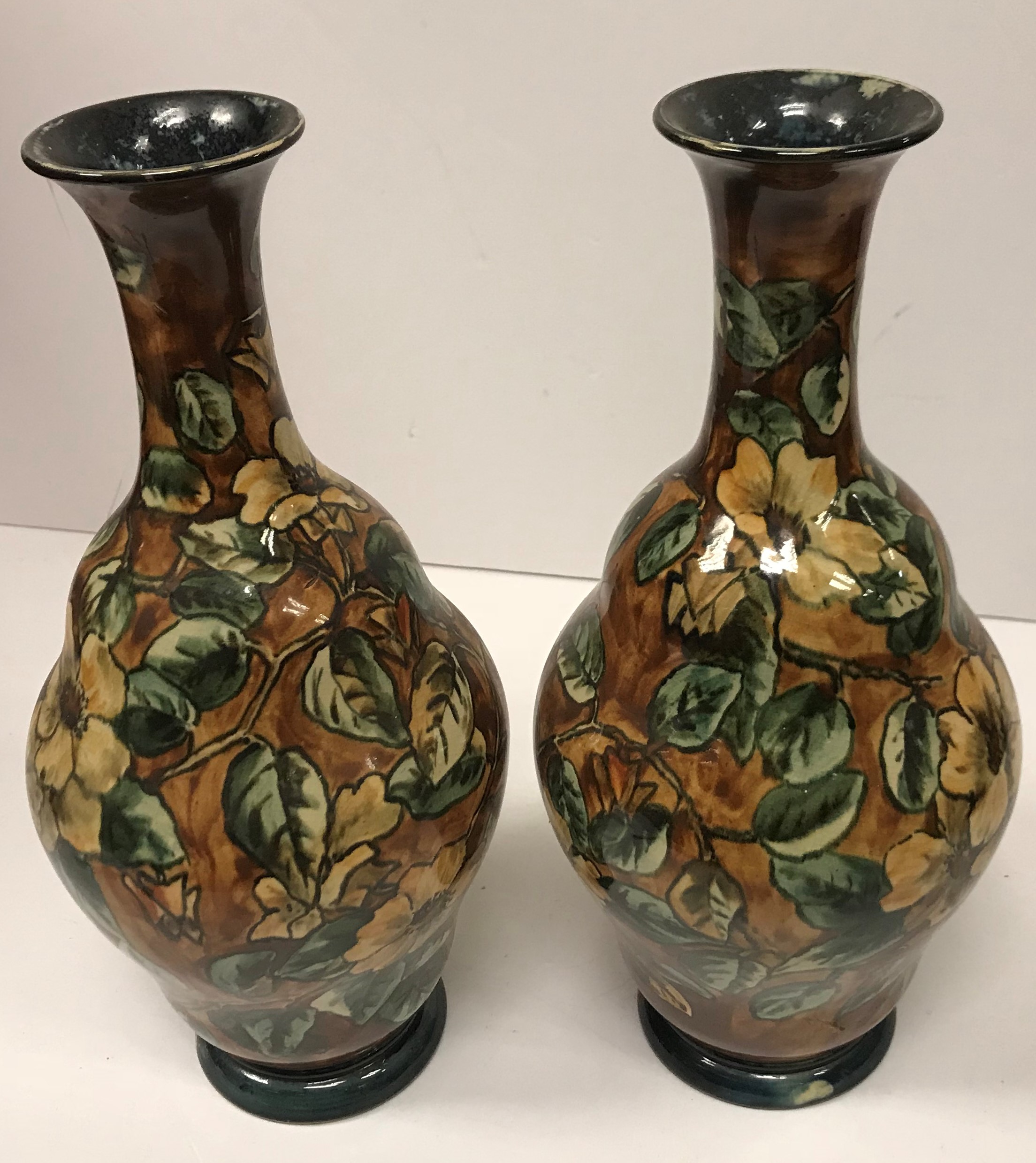 A pair of Doulton Lambeth faience ware vases, the brown ground set with floral decoration,