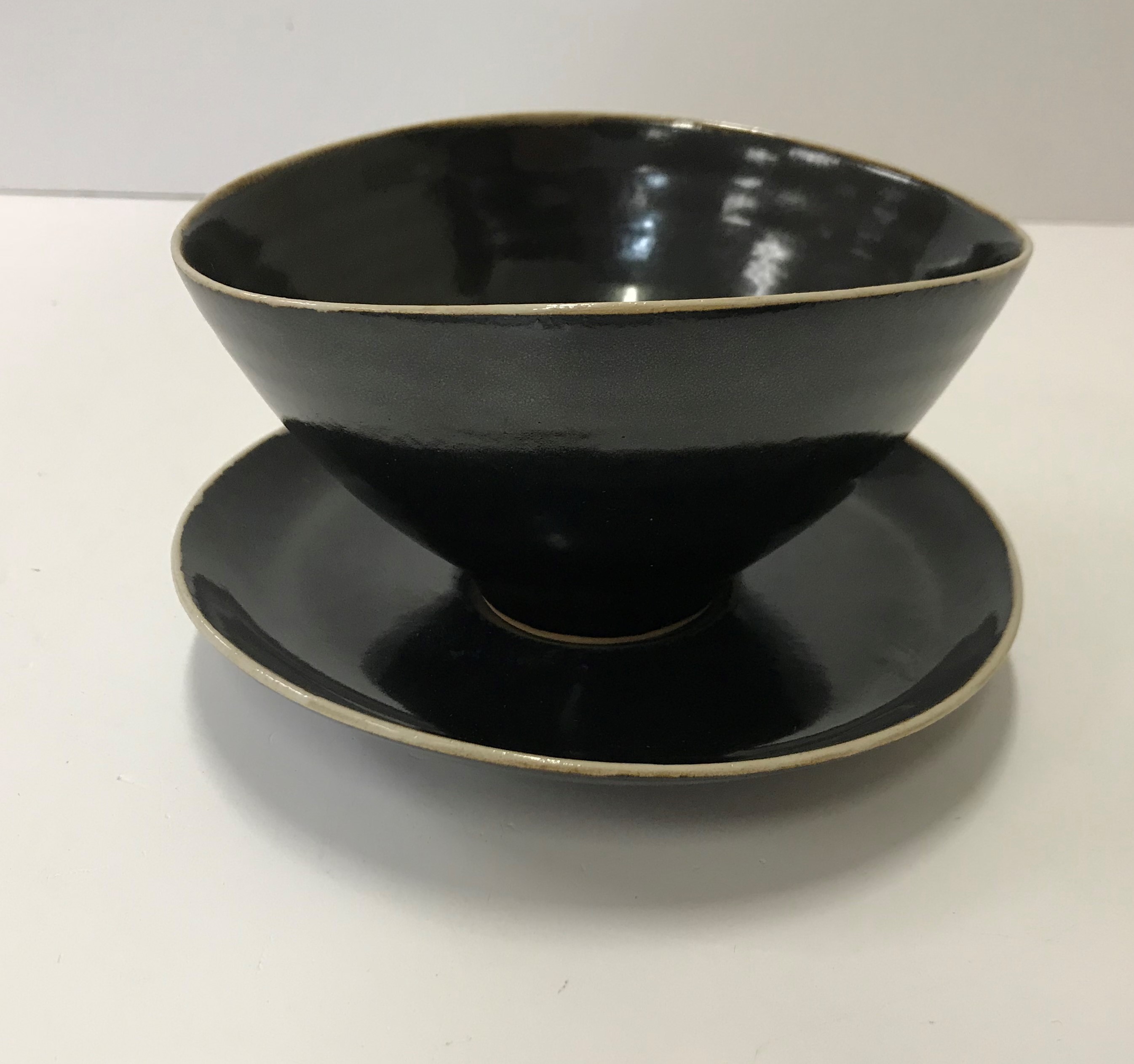 A Lucie Rie black glazed elliptical bowl and saucer, both bearing Lucie Rie marks,