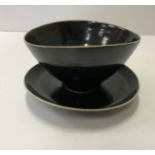 A Lucie Rie black glazed elliptical bowl and saucer, both bearing Lucie Rie marks,