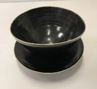 A Lucie Rie black glazed elliptical bowl and saucer, both bearing Lucie Rie marks 14 cm x 12.