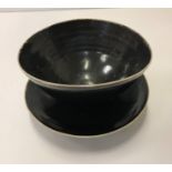 A Lucie Rie black glazed elliptical bowl and saucer, both bearing Lucie Rie marks 14 cm x 12.