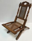 A Victorian child's folding caned campaign style chair with acanthus carved scrollwork top rail on