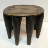 An Ashanti tribal stool with incised decoration to seat, raised on eight tapering legs,