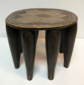 An Ashanti tribal stool with incised decoration to seat, raised on eight tapering legs,