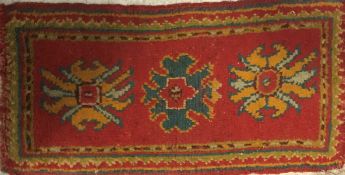 A Turkish rug, the central panel set with three stylised floral medallions on a red ground,