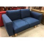 A modern blue upholstered two seat sofa with pockets to arms, raised on turned beech legs,