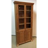 A modern pine cabinet with two glazed doors enclosing three shelves over two fielded panel doors
