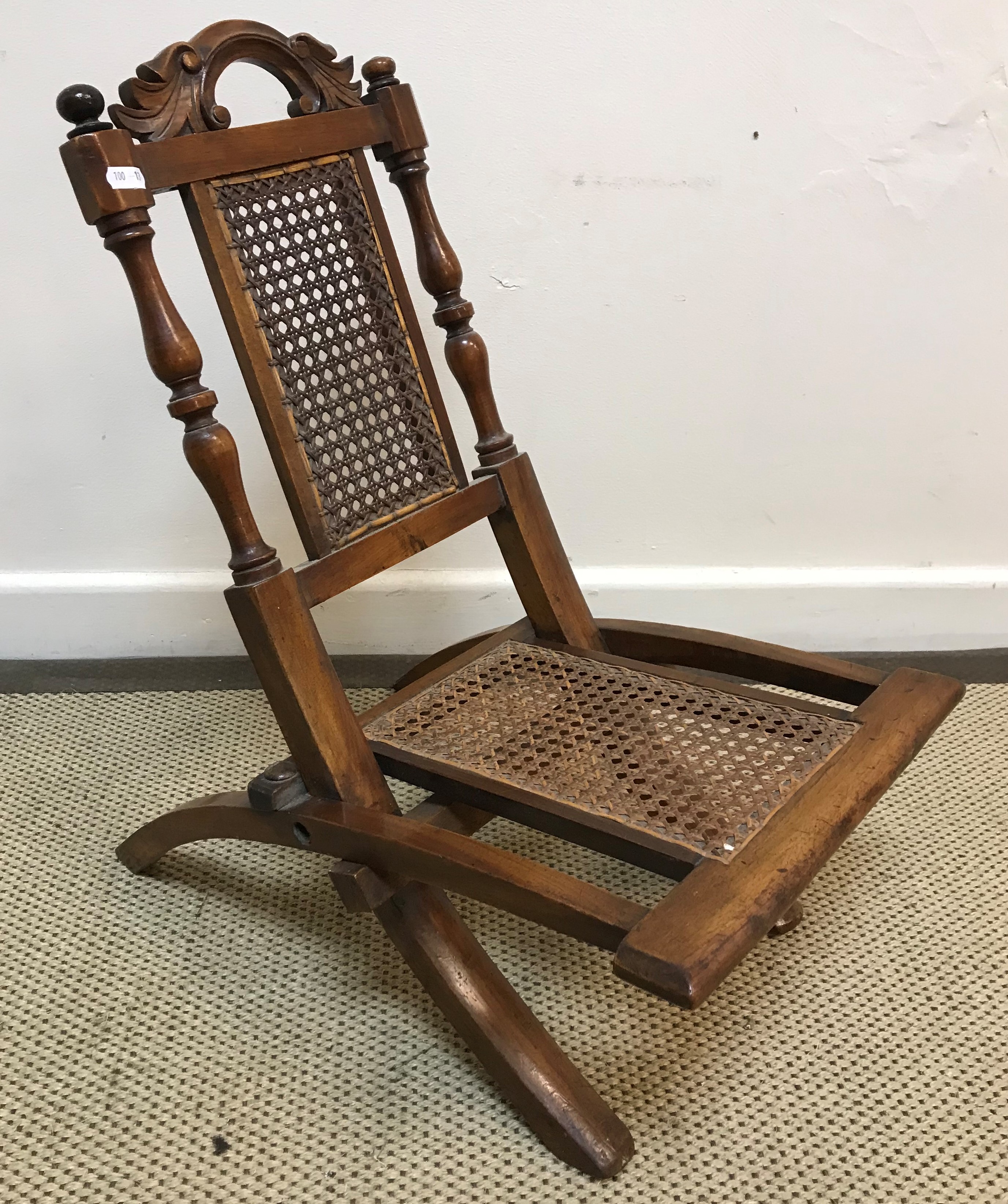 A Victorian child's folding caned campaign style chair with acanthus carved scrollwork top rail on
