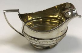 A late George III silver cream jug with lozenge engraved facet banded decoration raised on an oval