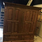 A modern pine double wardrobe with two pairs of fielded panelled doors enclosing hanging spaces,