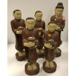 A carved and painted collection of five Tibetan figures of disciples or monks with food bowls in