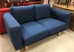 A modern blue upholstered two seat sofa with pockets to arms, raised on turned beech legs,