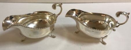 A pair of Edwardian silver sauce boats with dragooned edge raised on three hoof feet (Sheffield,