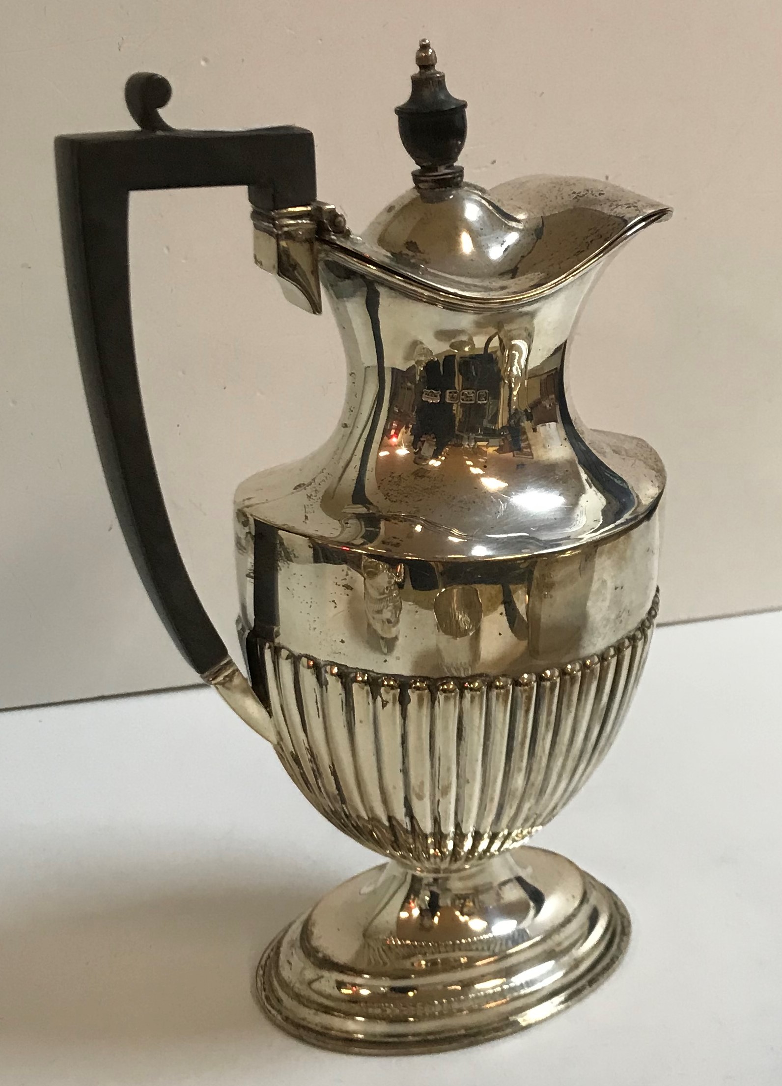 A George V silver hot water pot with reeded body raised on a stepped oval base with ebonised finial
