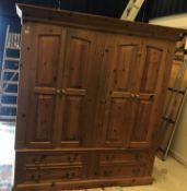A modern pine double wardrobe with two pairs of fielded panelled doors enclosing hanging spaces,