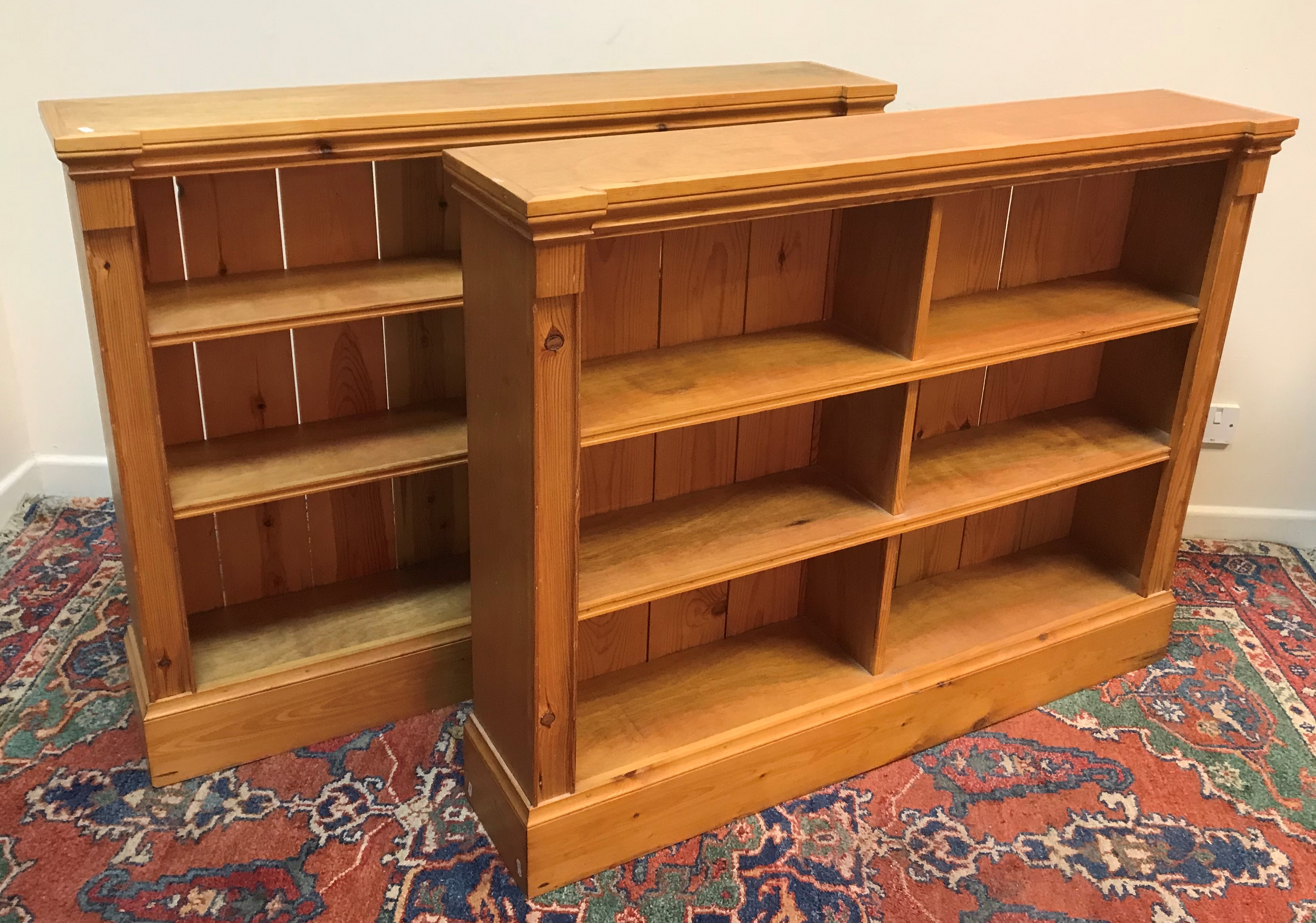 A pair of modern stained pine open bookcases of two banks of three shelves, raised on plinth bases,