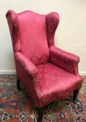 A circa 1900 upholstered wingback scroll arm chair with serpentine front seat rail on square