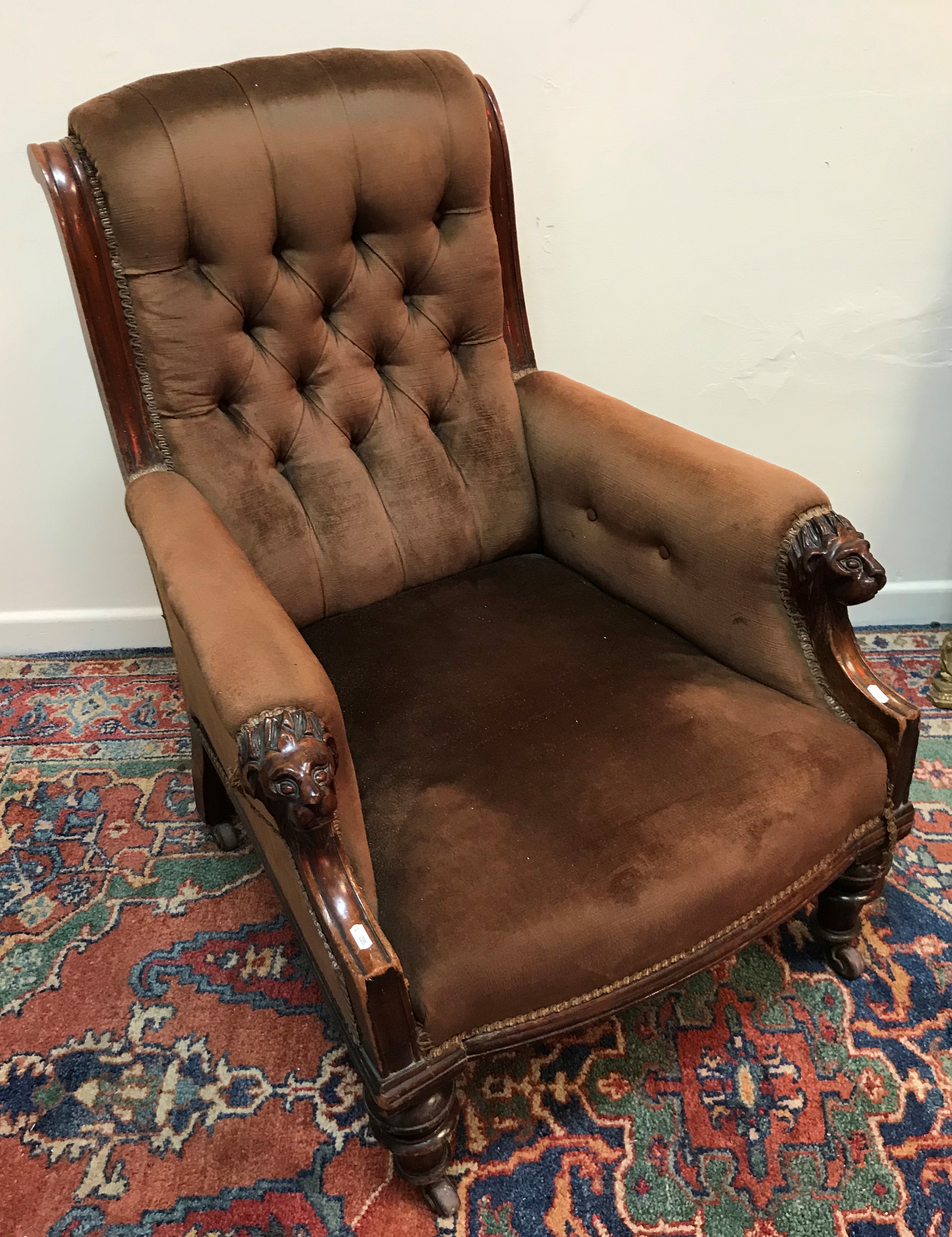 A Victorian mahogany framed button back salon arm chair with carved lion mask capped arm supports