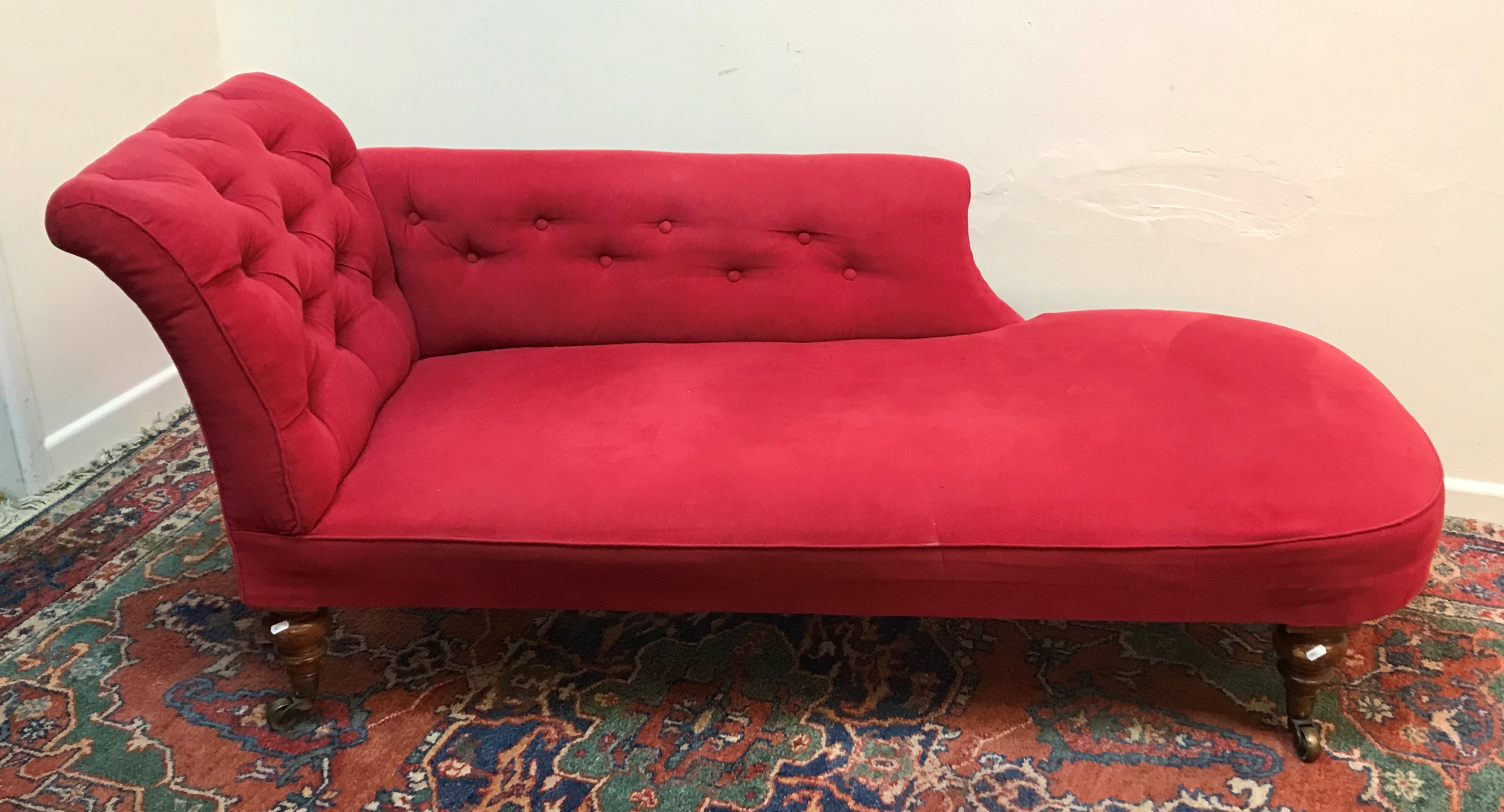 A Victorian buttoned upholstered scroll back chaise longue on turned legs to brass caps and castors