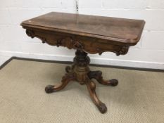 A Victorian walnut fold-over card table on centre pedestal to quadruped base and scroll feet,