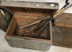 A wooden trunk containing various vintage hand tools comprising an adze, two scythes,