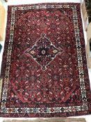 A Persian carpet, the central panel set with diamond shaped medallion on a red ground,
