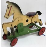 An early 20th Century wooden painted spring-loaded rocking horse toy on wheels bearing remains of