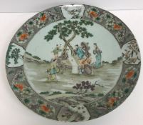 A Kangxi porcelain charger decorated with figures around a table in a garden setting within a