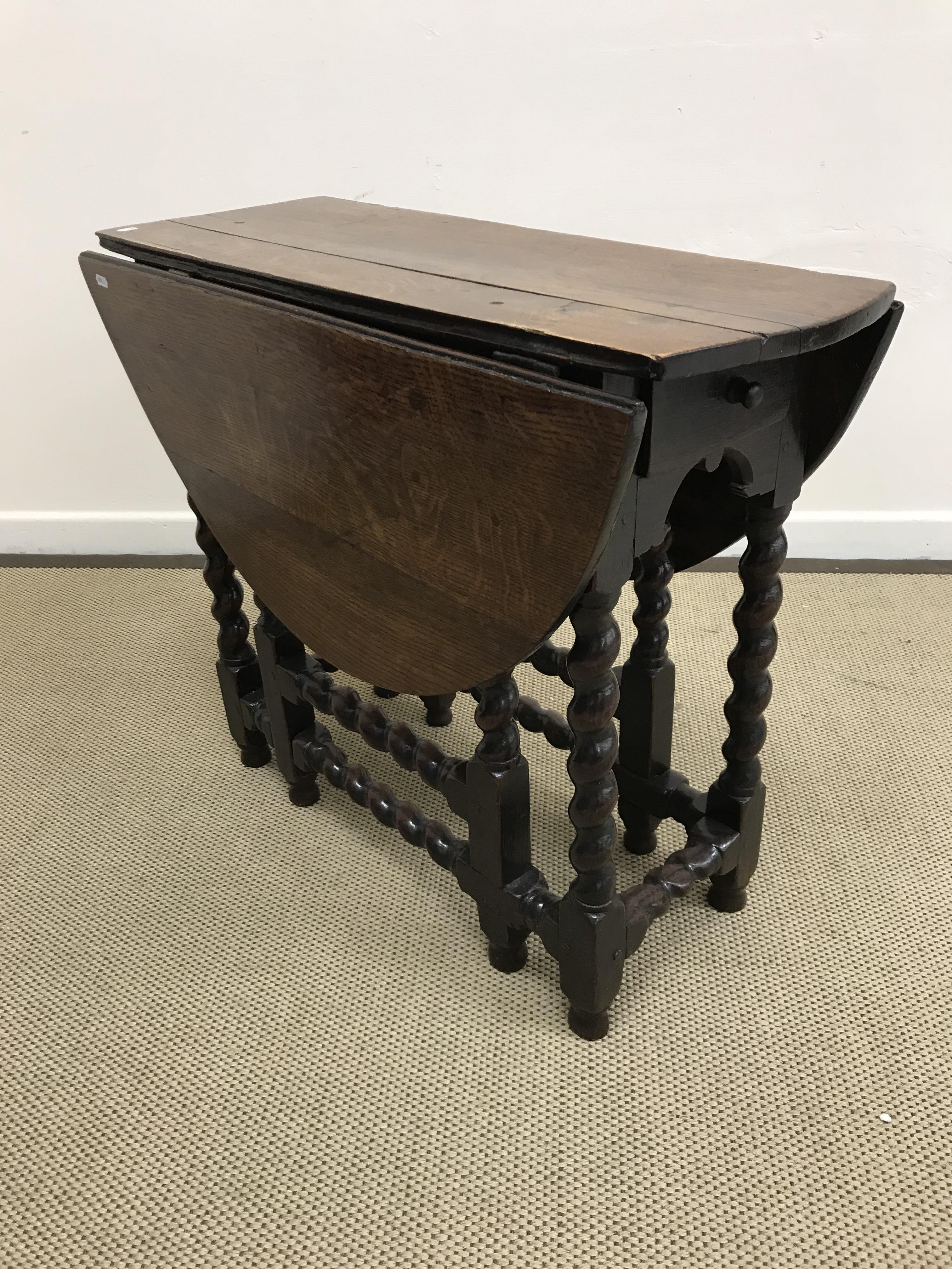 An 18th Century oak oval gate-leg drop-leaf dining table on barley-twist supports united by