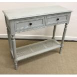 A modern grey painted two drawer side table on turned legs united by a caned under tier 91 cm wide
