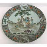 A Kangxi style porcelain charger decorated with figures around a table in a garden setting within a