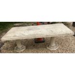 A cast concrete garden table raised on two pillars,