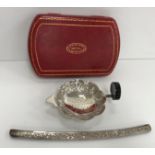 An Eastern (possibly Thai or Burmese) embossed white metal tea strainer and stand with figural and