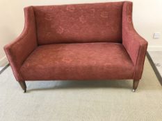 An Edwardian upholstered swept arm two seat sofa on square tapered front legs to castors,