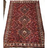 A Persian carpet, the central panel set with three repeating medallions on a red ground,