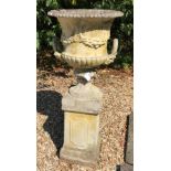 A composite stone garden urn with swag decoration and twin handles, raised on a pedestal base,