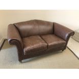 A Laura Ashley "Gloucester" brown leather upholstered scroll arm two seat sofa on turned front legs