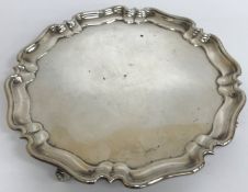 A silver salver in the Georgian manner with pie crust rim raised on four scroll feet,