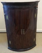 An early 19th Century mahogany bow fronted corner cupboard, the top with blind fretwork decoration,