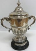 A silver lidded trophy cup with two scroll work handles and mask and shell decorated relief work