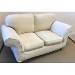 A modern two seat cream sofa, raised on turned mahogany front legs to brass caps and castors,