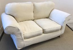 A modern two seat cream sofa, raised on turned mahogany front legs to brass caps and castors,