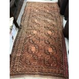 A Bokhara rug, the central panel set with two rows of repeating medallions on a rust ground,
