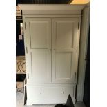 A modern cream painted pine wardrobe with two doors enclosing a hanging space and adjustable shelf