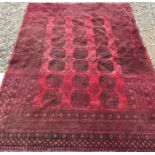 A Bokhara rug, the central panel set with three rows of repeating medallions on a dark red ground,