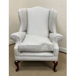 A wing back armchair in the 19th Century taste raised on cabriole legs to pad feet,