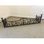A wrought iron scrollwork decorated fire fender with central flower head medallion and ball end