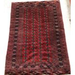 A Bokhara rug, the central panel set with repeating elephant foot medallions on a dark red ground,