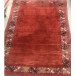 A Persian rug, the plain red ground set with a border of geometric blue and cream design approx.